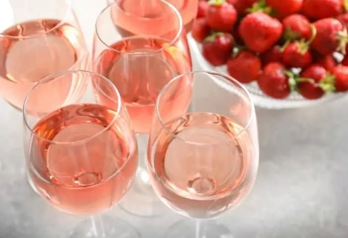 glasses of strawberry wine and a bowl of strawberries - How to Make Strawberry Wine Step-By-Step - Stone Family Farmstead